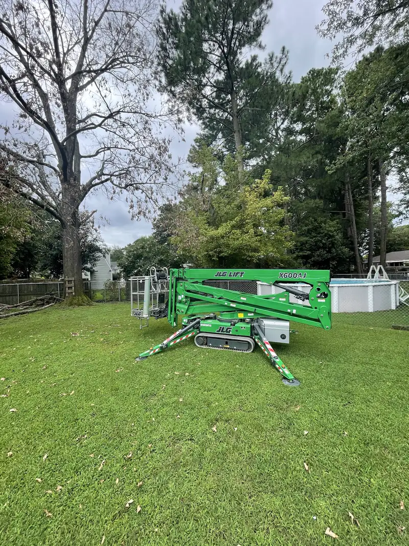 Their green tracked spider lift set up on a back lawn under tall trees